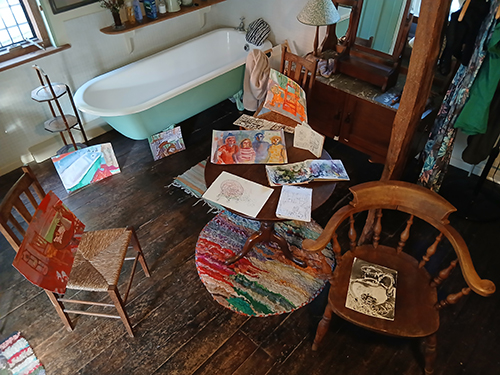 A room with a bath in it and some paintings on chairs